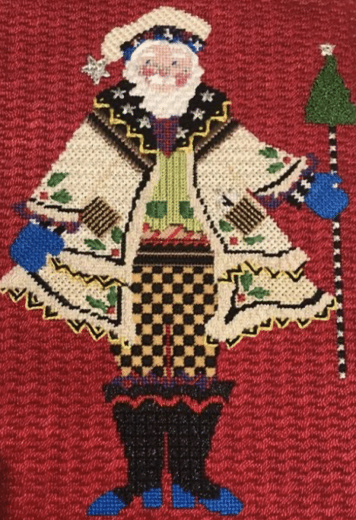 Santa figure in a white coat, checked pants, and black boots holding a staff with a Christmas tree on top. The stitch techniques will be taught in a needlework class on the 2022 summer vacation cruise.