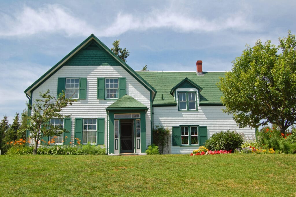 This White House with a green roof and trip is the Anne of Green Gables house in Prince Edward Island, Canada. Prince Edward Island is a port of call on the Stitchers' Escapes 2023 fall needlework cruise.